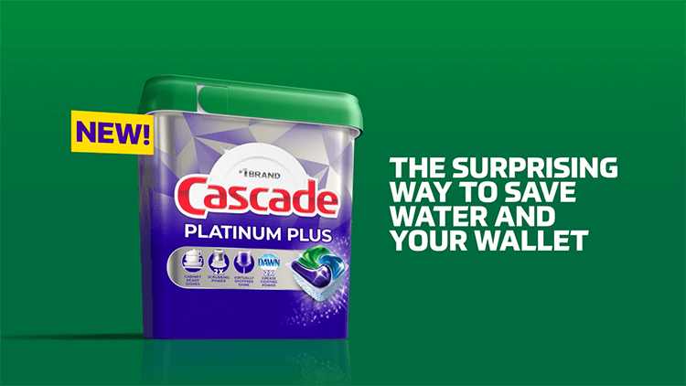 A blue, green and white plastic box. The front label displays a dishwashing detergent pod with the name Cascade Platinum Plus in red and white text. The box is displayed against a green background.