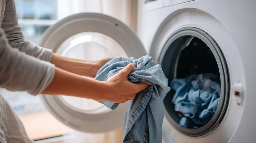 A person places denim garments into a washing machine drum