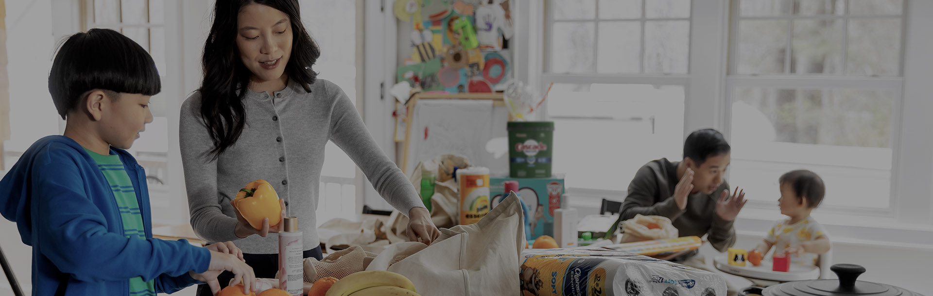 Family of four in the kitchen talking and storing groceries