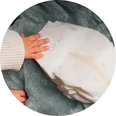 A close-up of a baby's hand resting on the soft waistband of a Pampers AMORE diaper, demonstrating its gentle and premium feel.