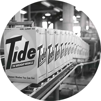 A black and white image of boxes of Tide move down the manufacturing line in 1965.