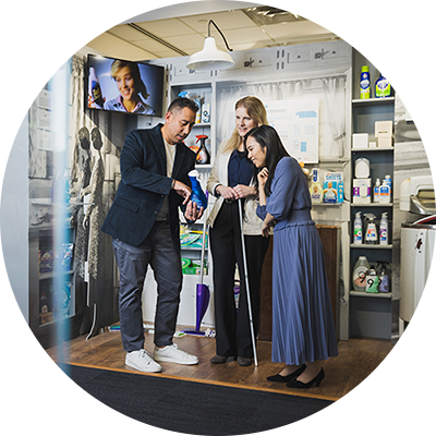 A Hispanic male, white female and Asian female stand in a mid-century model laundry room. They are looking at a blue dish detergent bottle that the male employee is holding.