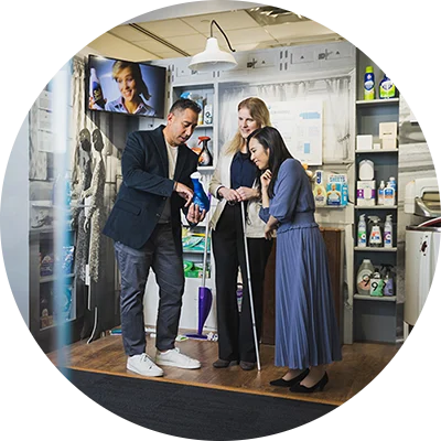 A Hispanic male, white female and Asian female stand in a mid-century model laundry room. They are looking at a blue dish detergent bottle that the male employee is holding.