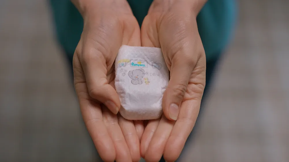 A close-up of a pair of cupped hands carefully holding the Pampers Preemie Swaddlers Pxxs, the world's tiniest diaper, emphasizing its delicate scale and the care behind the innovation.