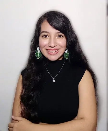 A young Hispanic women with long dark hair, green earrings and a black sleeveless sweater smiles and poses for a headshot.