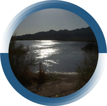 A body of water surrounded by trees. The sun is shining on the water.