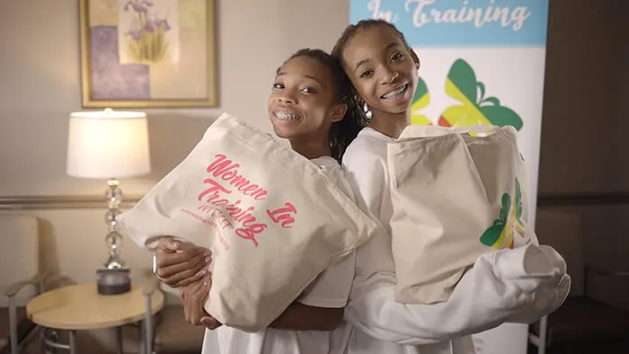 13-year-old sisters Brooke and Breanna Bennett stand back-to-back holding Women In Training donation bags
