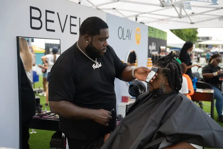 Black consumers experience innovative brands at My Black Is Beautiful, Olay and Bevel stations during the HBCYOU Tour. In the inset, a Black man is seated in a chair and receives a haircut from a barber.