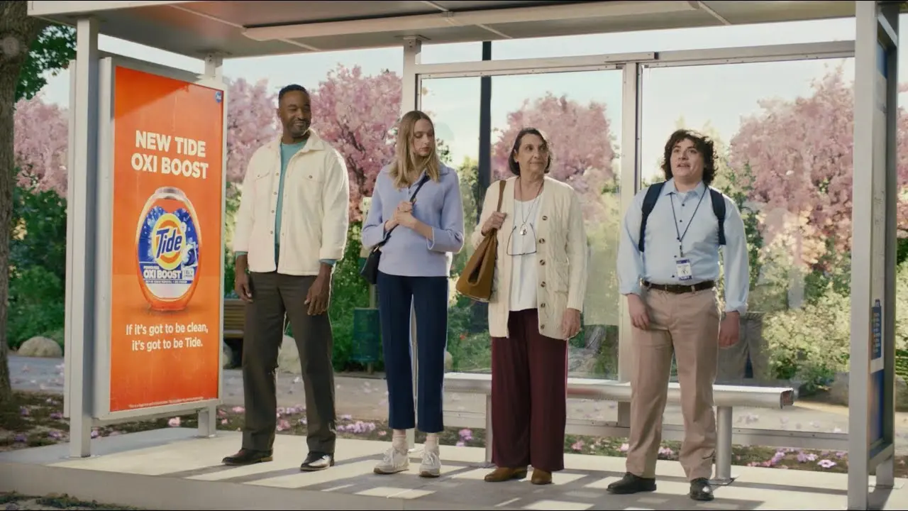 Two women and two men dressed in work attire wait at a bus stop that features a Tide Oxi Boost ad.