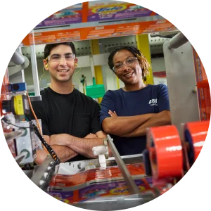Woman and a man standing with their arms crossed and smiling next to a Tide production line