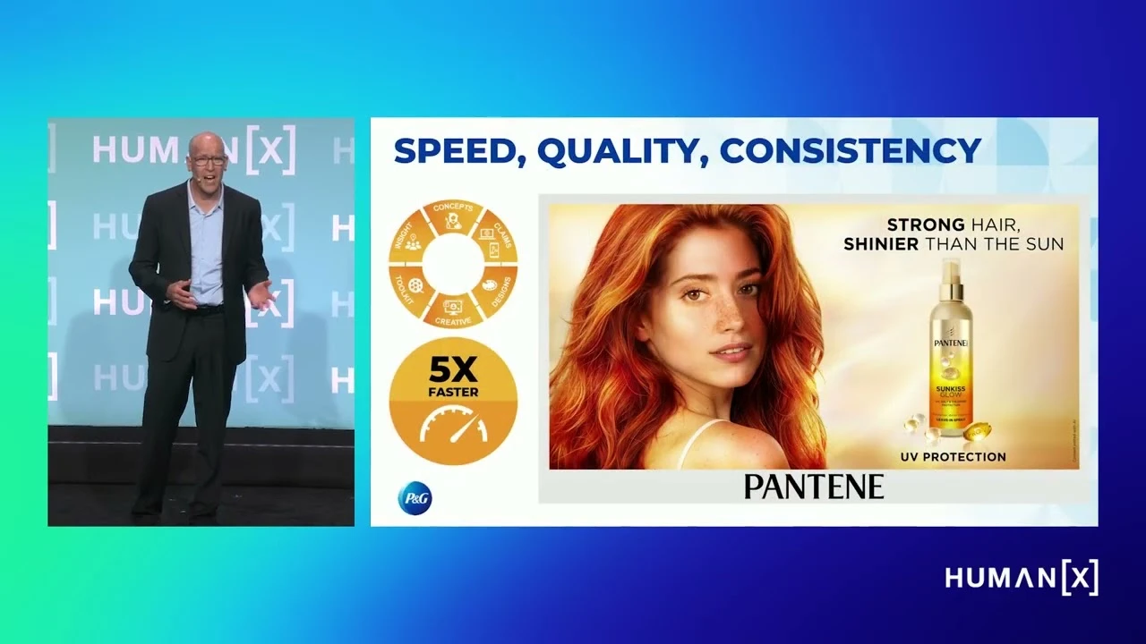 A man in a blue shirt and black suit speaks onstage. An image of a woman with red hair and a bottle of hair product is next to him.