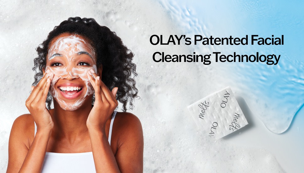 A woman is smiling and washing her face and an OLAY Cleansing Melts tile is shown in front of a blue and white background. Text on screen reads “OLAY’s Patented Facial Cleansing Technology