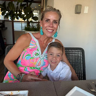 A mother and her young son smile brightly for the camera while dining outdoors.