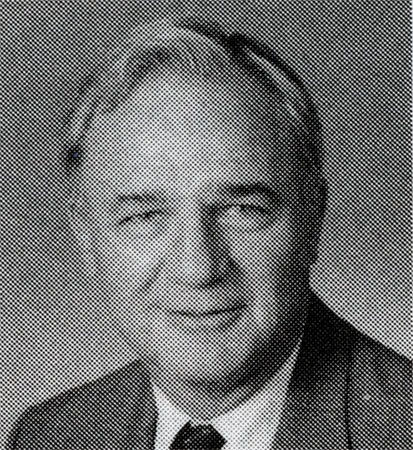 Black and white photo of a man in a white shirt, tie and suit jacket.