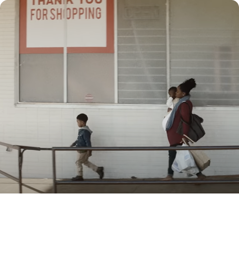 Screenshot from Widen the Screen movie. Woman walking and holding her child in her arms. Her second child walking in front of her.