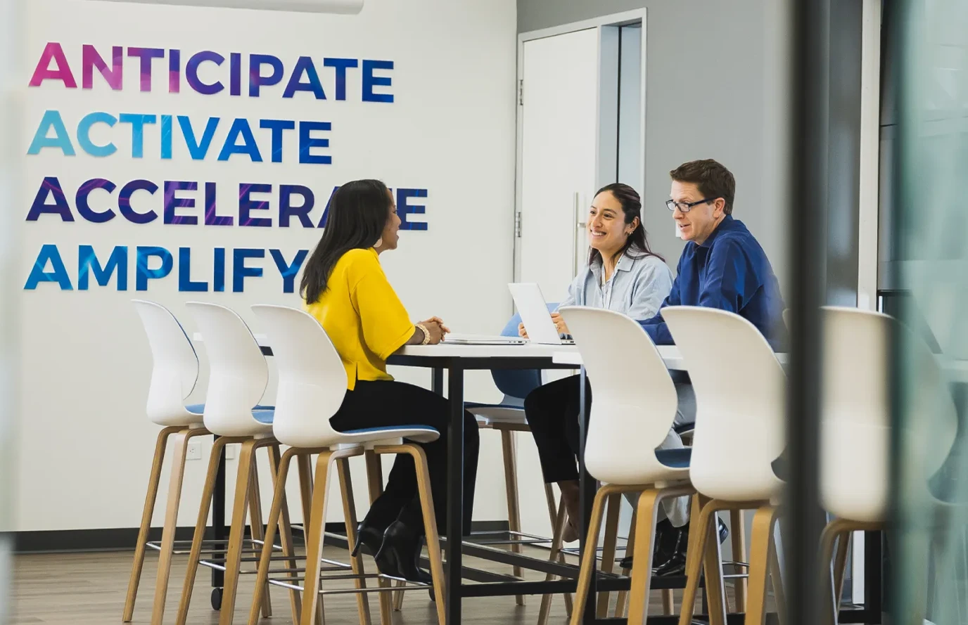 Group of P&G coworkers seated at a high‑top table in a bright office space.