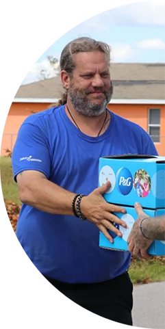 A man with a beard smiling and handing P&G branded boxes to someone in need.