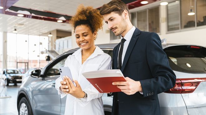 Woman and man in dealership with cell phone and deal jacket