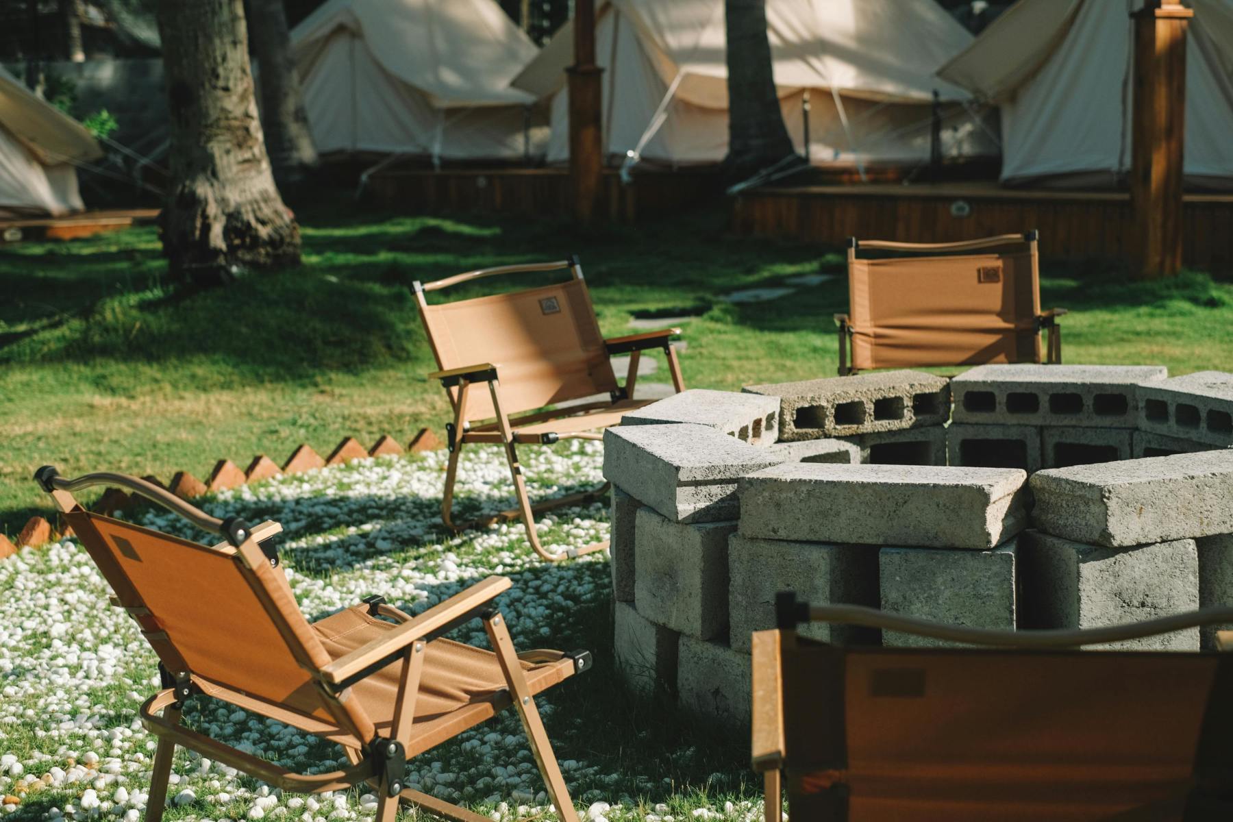 A tranquil camping spot featuring a cozy fire pit surrounded by folding chairs, with glamping tents nestled in the background