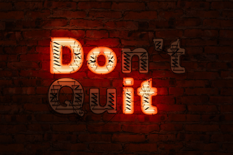 a neon sign on a dark brick wall that says "don't quit" . The illuminated letters spell out "Do It".