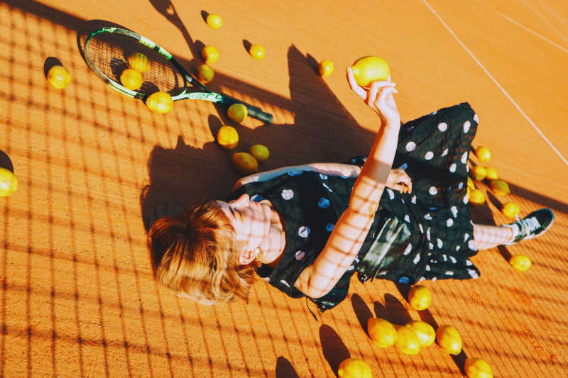 Women laying on tennis court surrounded by lemons