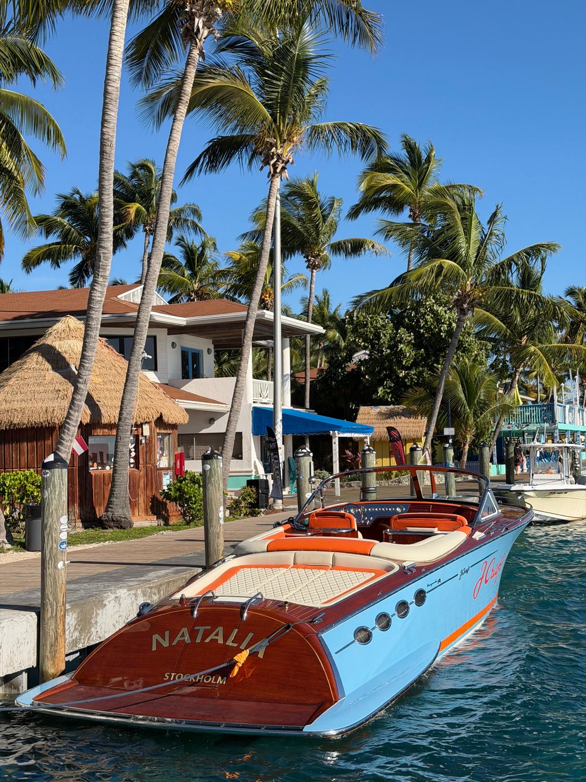 J Craft Natalia docked stern-first at a tropical marina with signature mahogany transom and blue hull