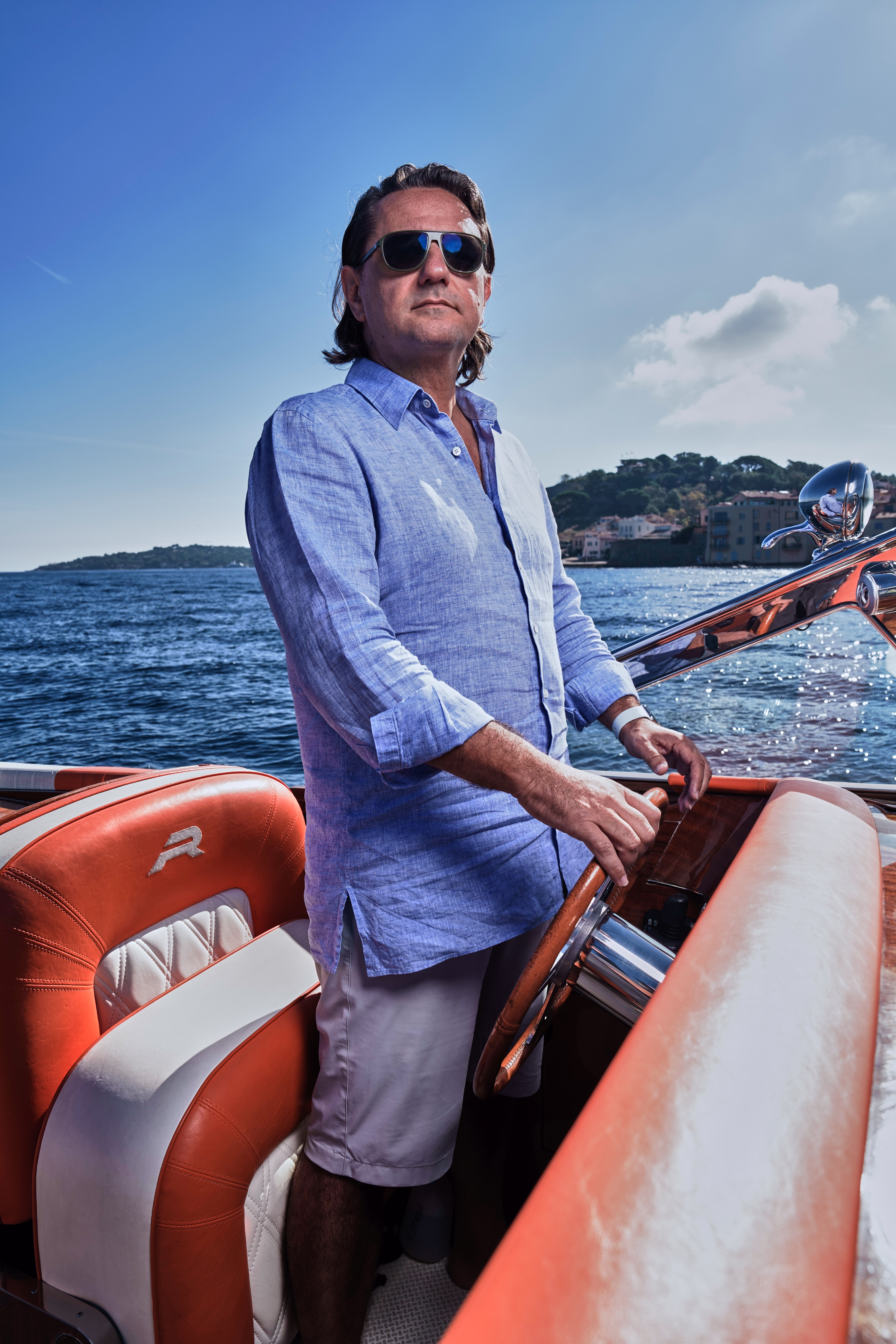 Captain in sunglasses at the helm of a J Craft Torpedo with Mediterranean coastline behind