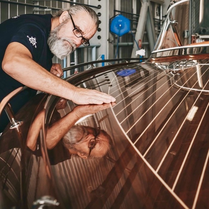 A J Craft craftsman working by hand on a high-gloss mahogany Torpedo deck.