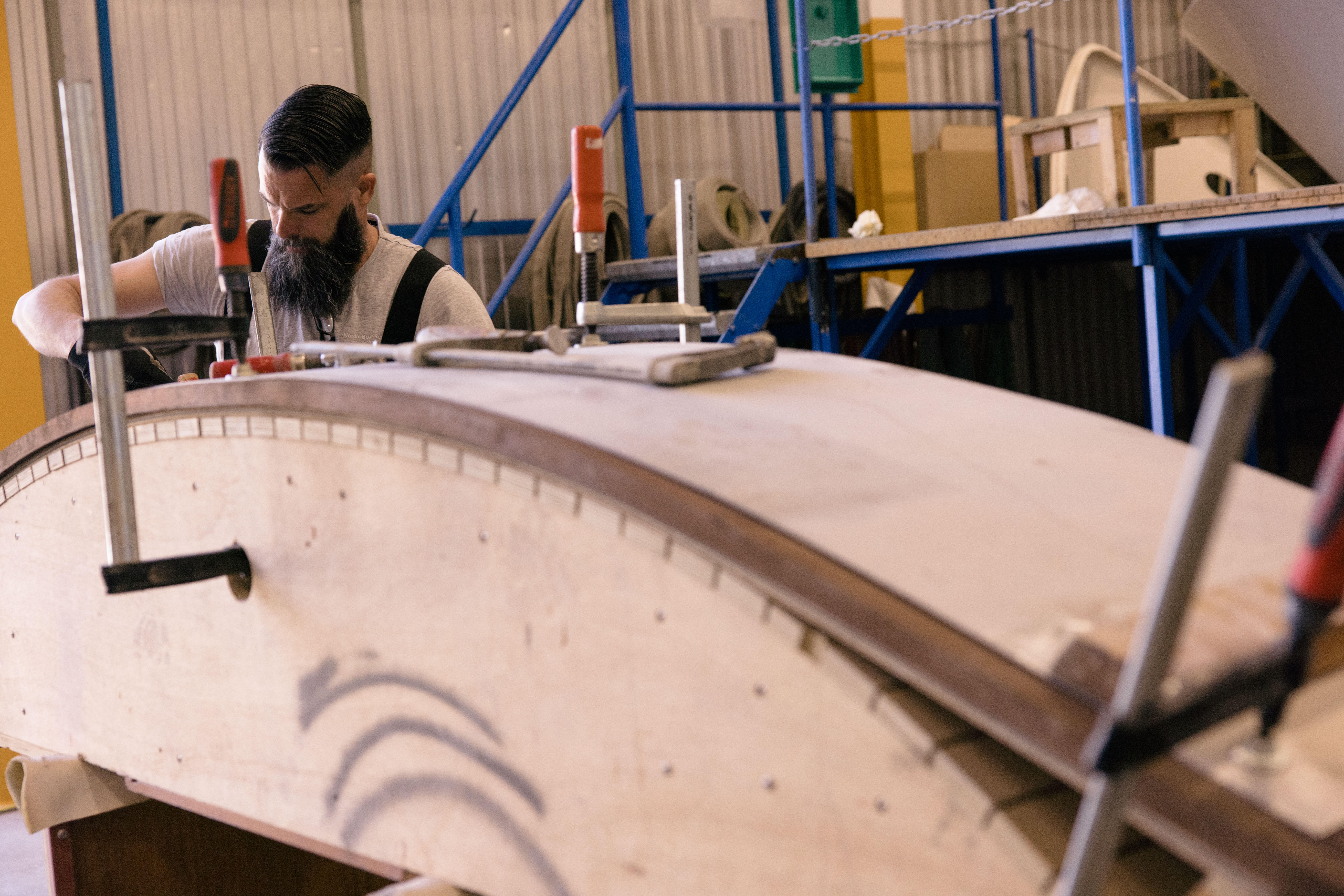 Craftsman using bar clamps to shape wood panels on a J Craft hull in the workshop