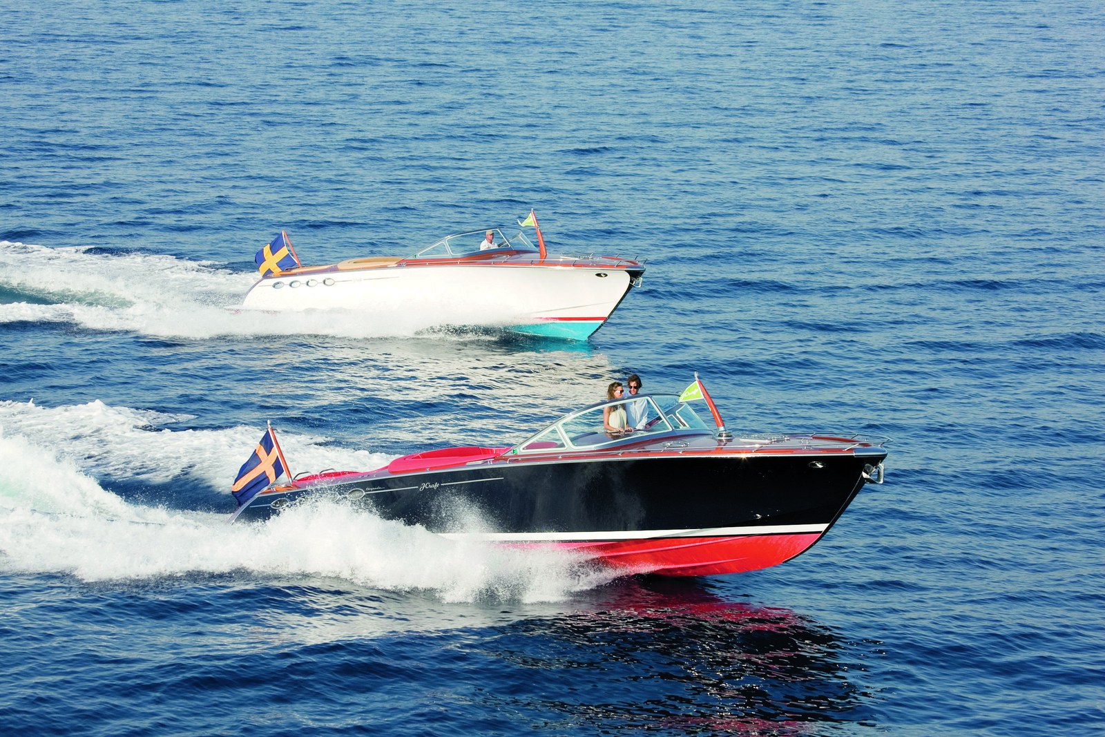 Two J Craft runabouts underway, showing the classic mahogany silhouette that connects the Cabrio Cruiser and Torpedo.