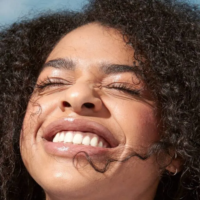 A portrait of a girl with very curly dark hair smiling and showing her face towards the sun