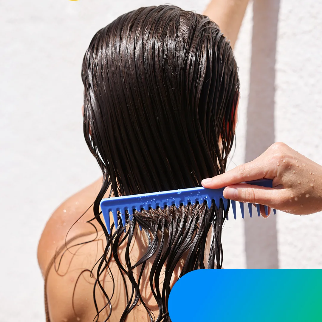 A woman with freshly washed hair stands under the shower, trying to comb it.