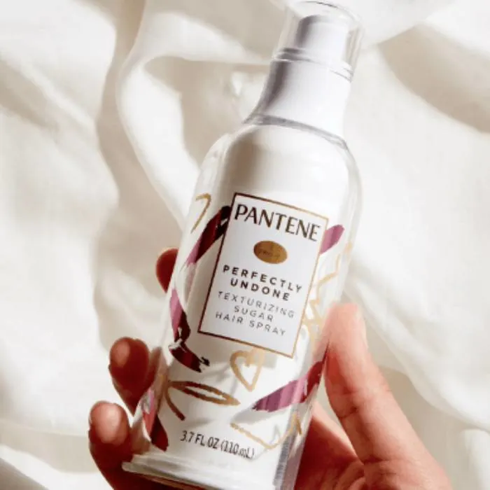 A photo of Pantene Hair Spray holded in woman's hand shown on the white fabric background