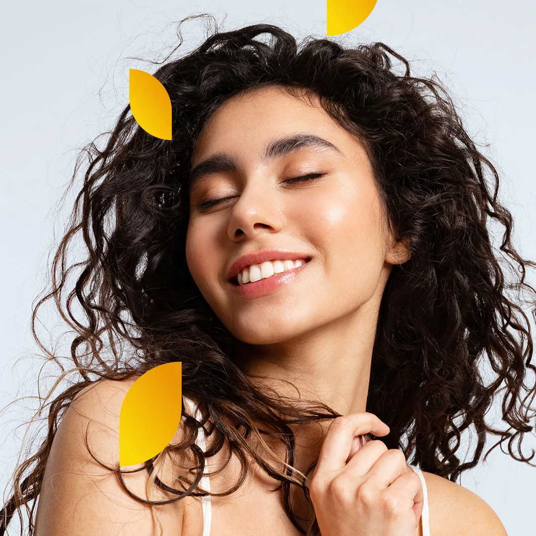 A woman with curly hair is facing sideways with her eyes closed, smiling.