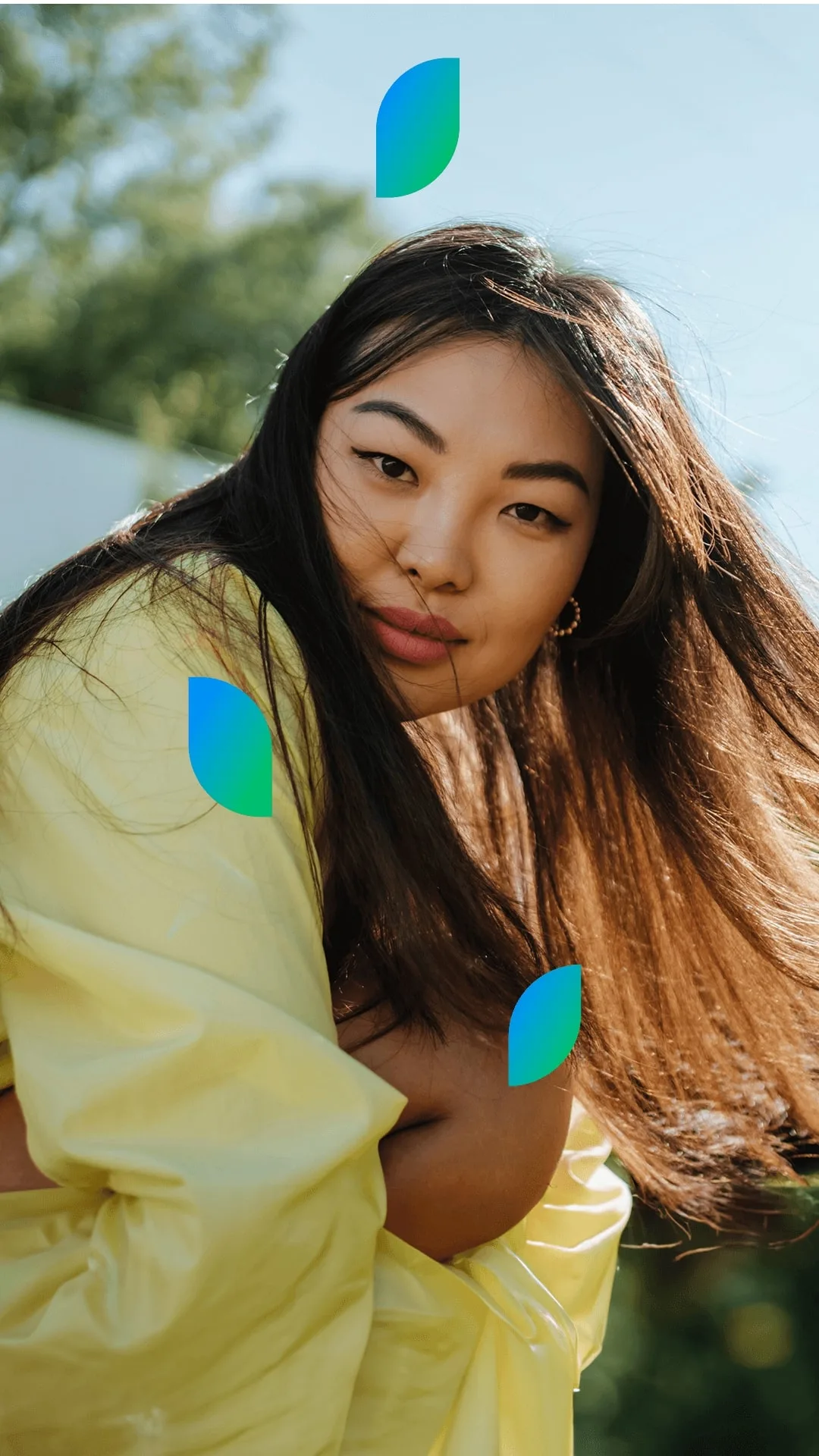 A woman with long, straight hair leans forward, her hair gently blowing in the breeze outdoors.