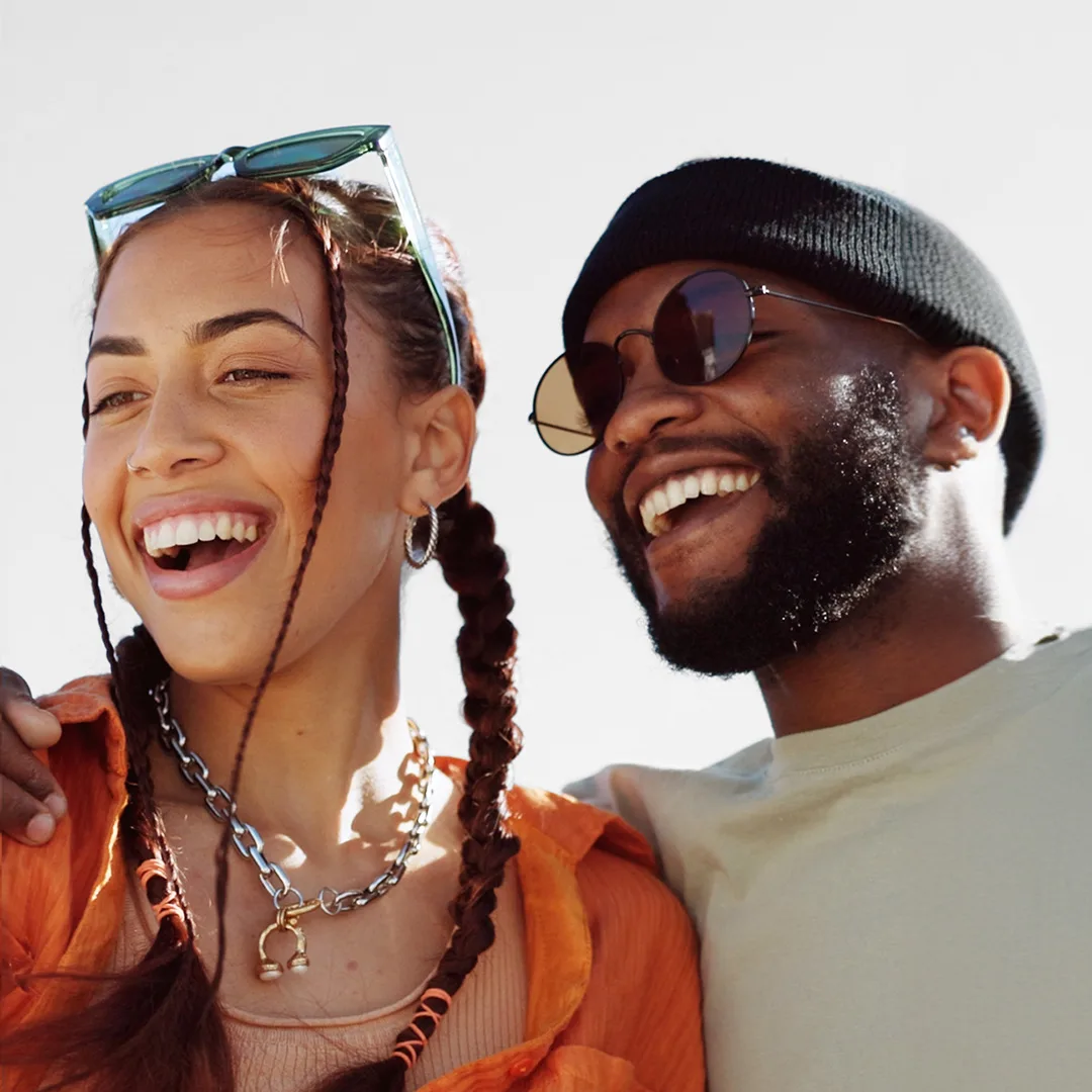 A woman and a man with different hairstyles are sitting next to each other, smiling.