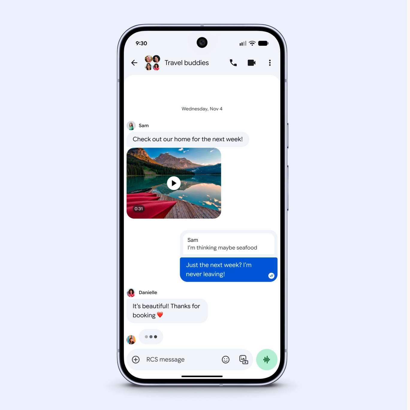 A screenshot of a "Travel buddies" group chat on a smartphone. A user named Sam shares a video of a scenic lake and mountains. A reply in a blue bubble reads, "Just the next week? I’m never leaving!" Another user, Danielle, replies, "It’s beautiful! Thanks for booking" with a red heart emoji.