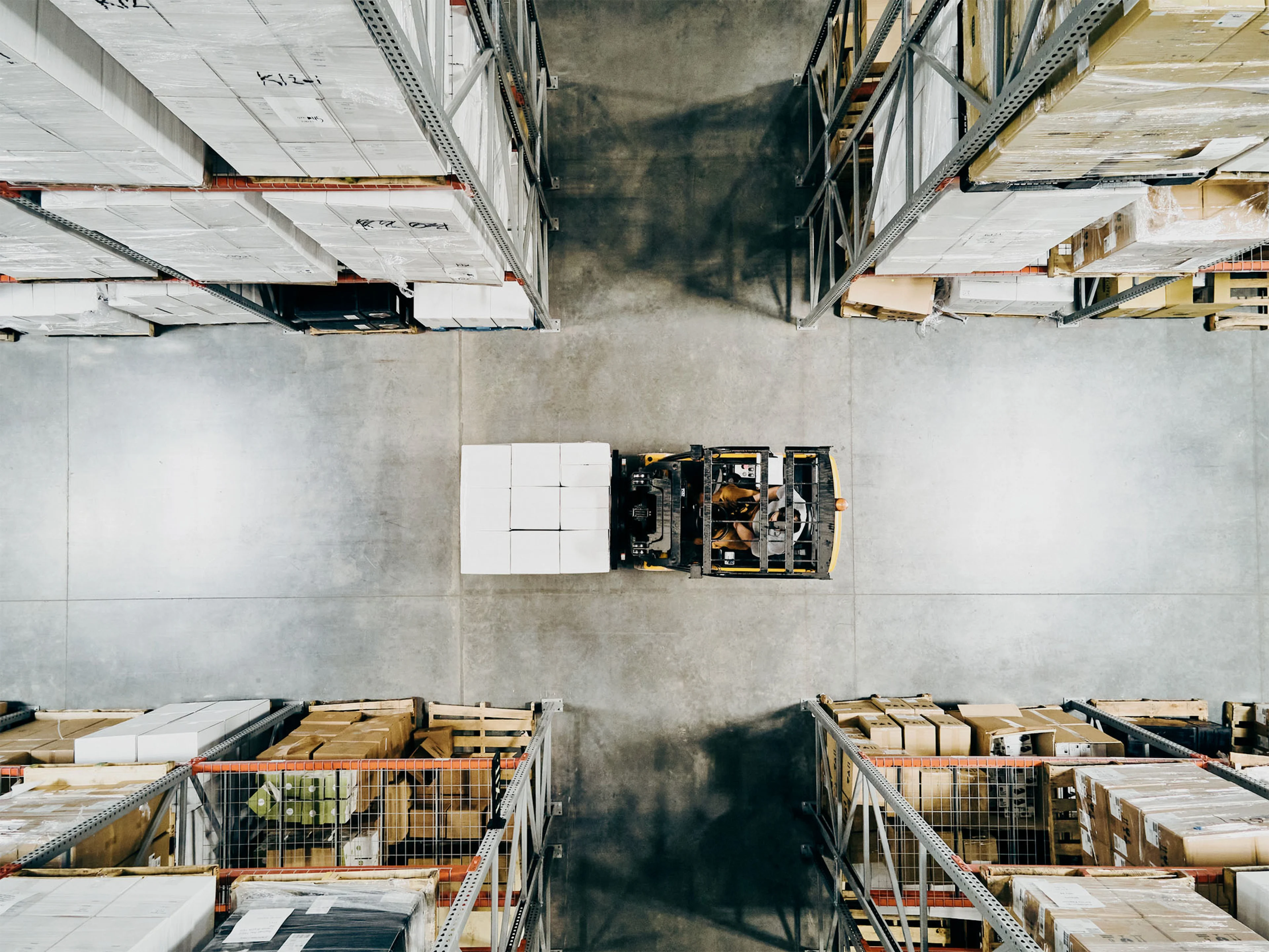 Overhead view of warehouse worker moving pallet of goods with forklift in warehouse.