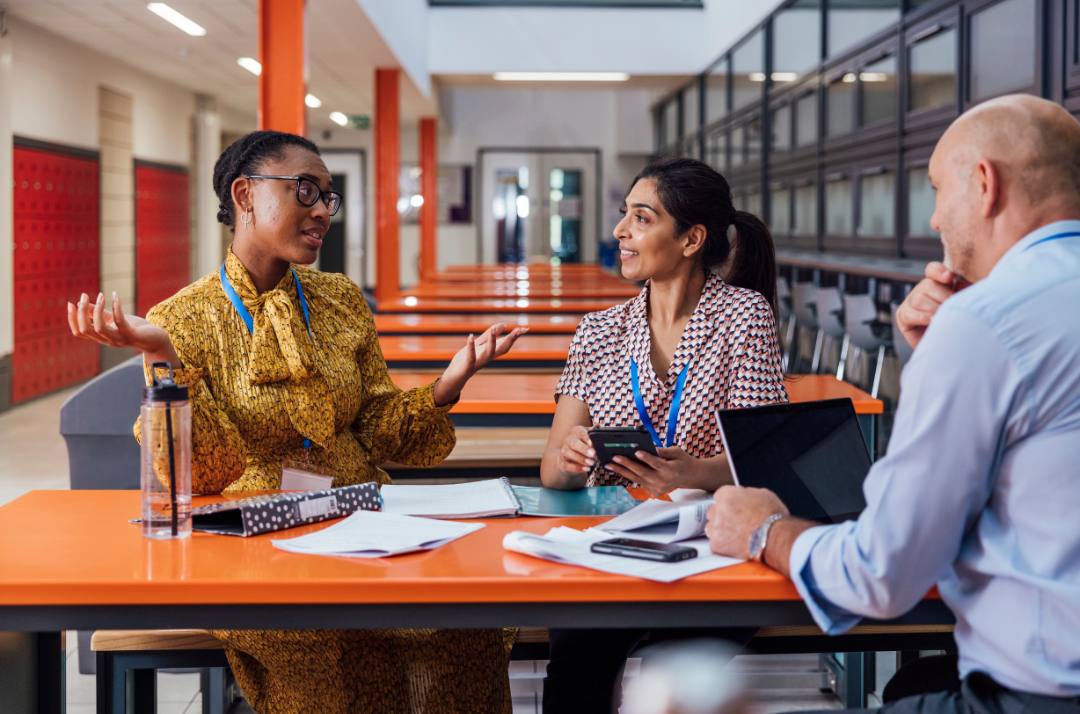 Two women and a man school Human Resources (HR) staff planning for retention for the next school year in a school multipurpose room.