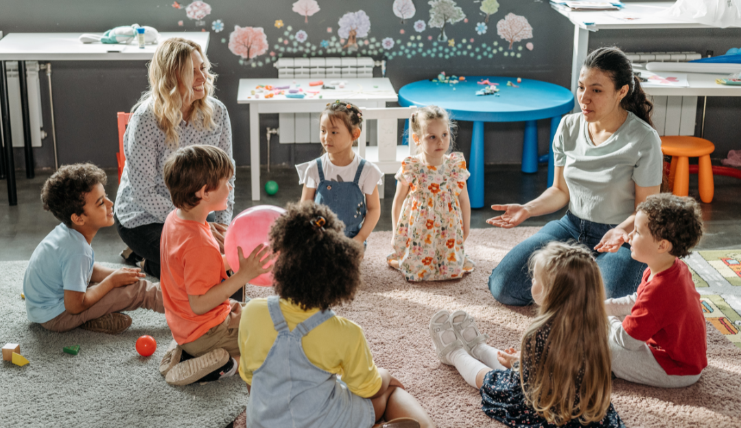 Mentor teacher and student teacher sitting on a classroom rug with young students.