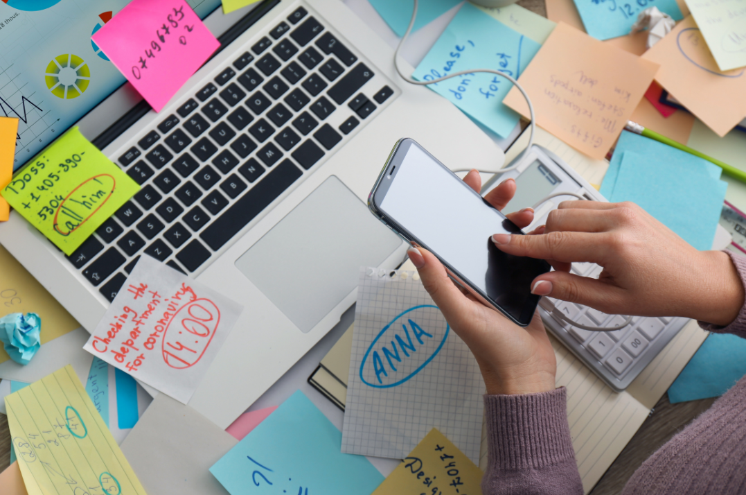 A person holding a phone over a messy desk.