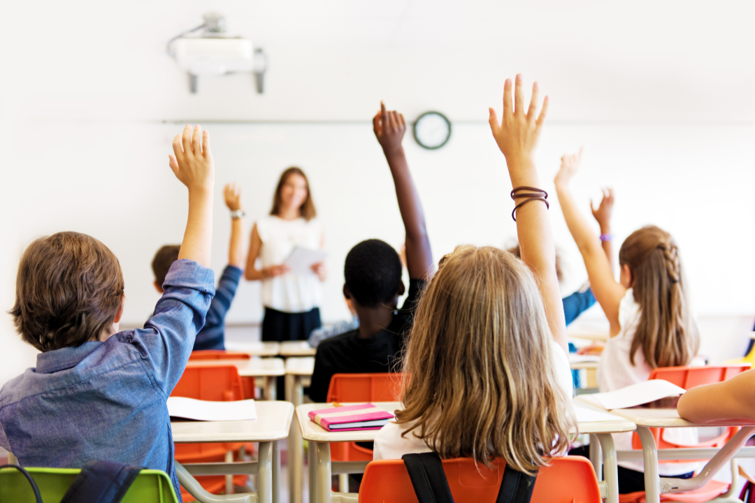 Students raising their hands in a classroom.