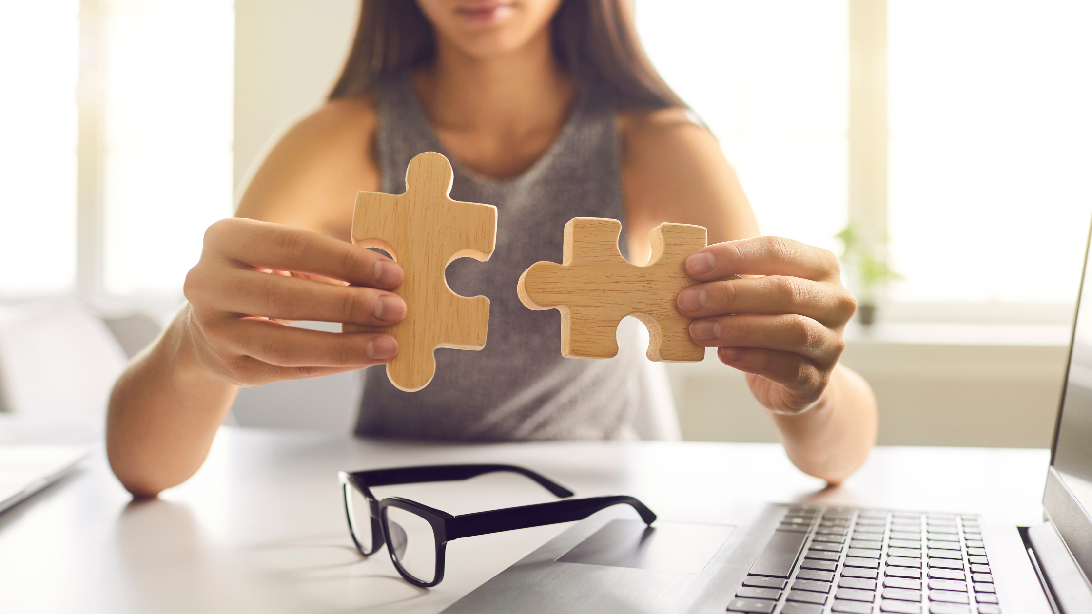 Woman holding two wooden puzzle pieces that will join together.