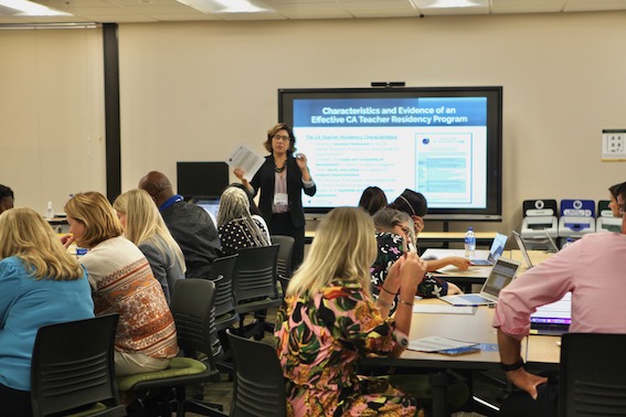 Jeanna Perry of the California Teacher Residency Lab standing in front of a projection presenting information to be an audience.