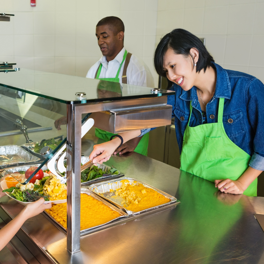 2 food service workers serving students at a school