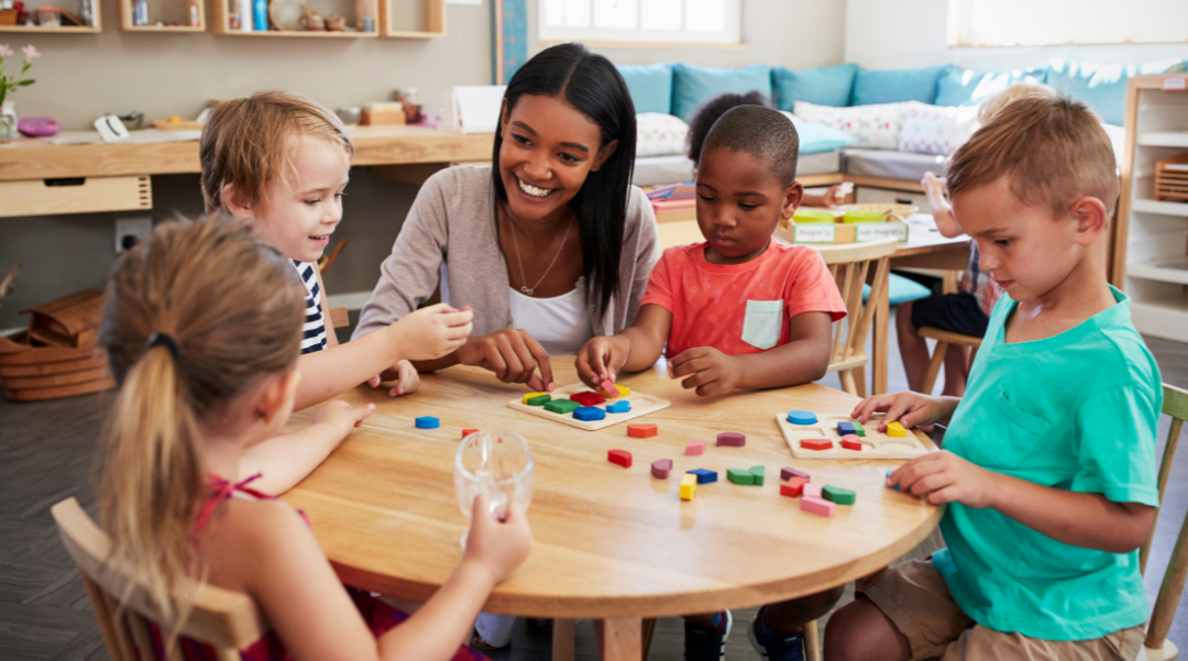 A Black woman teacher working with pre-school students at a table using manipulatives.