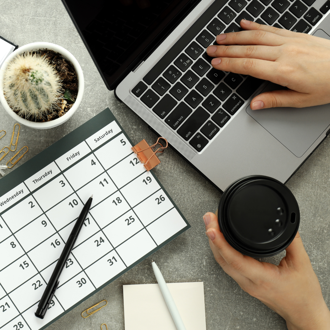 A person working on a laptop and holding a coffee at a desk with a calendar open getting ready to complete the Torace Timeline Planner.