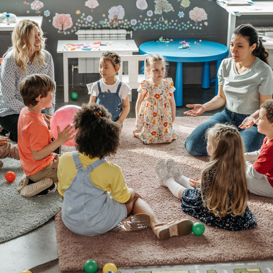 Mentor teacher and student teacher sitting on a classroom rug with young students.