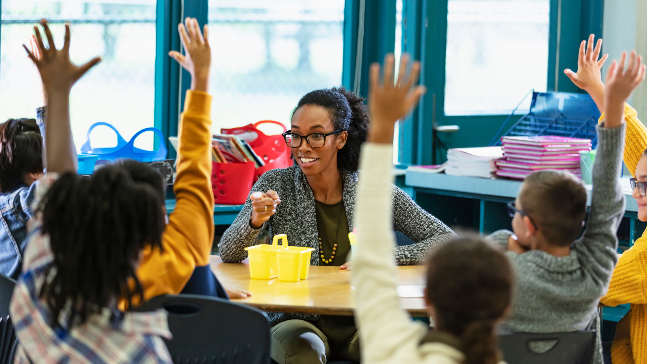 A young first-year teacher pointing into a crowd of students eagerly raising their hands.