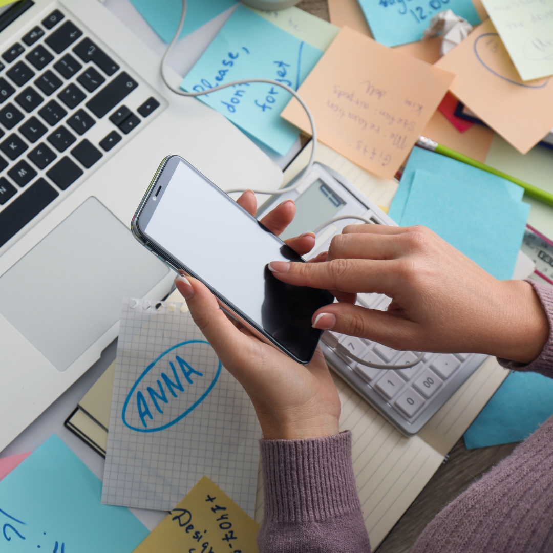 A person holding a phone over a messy desk.